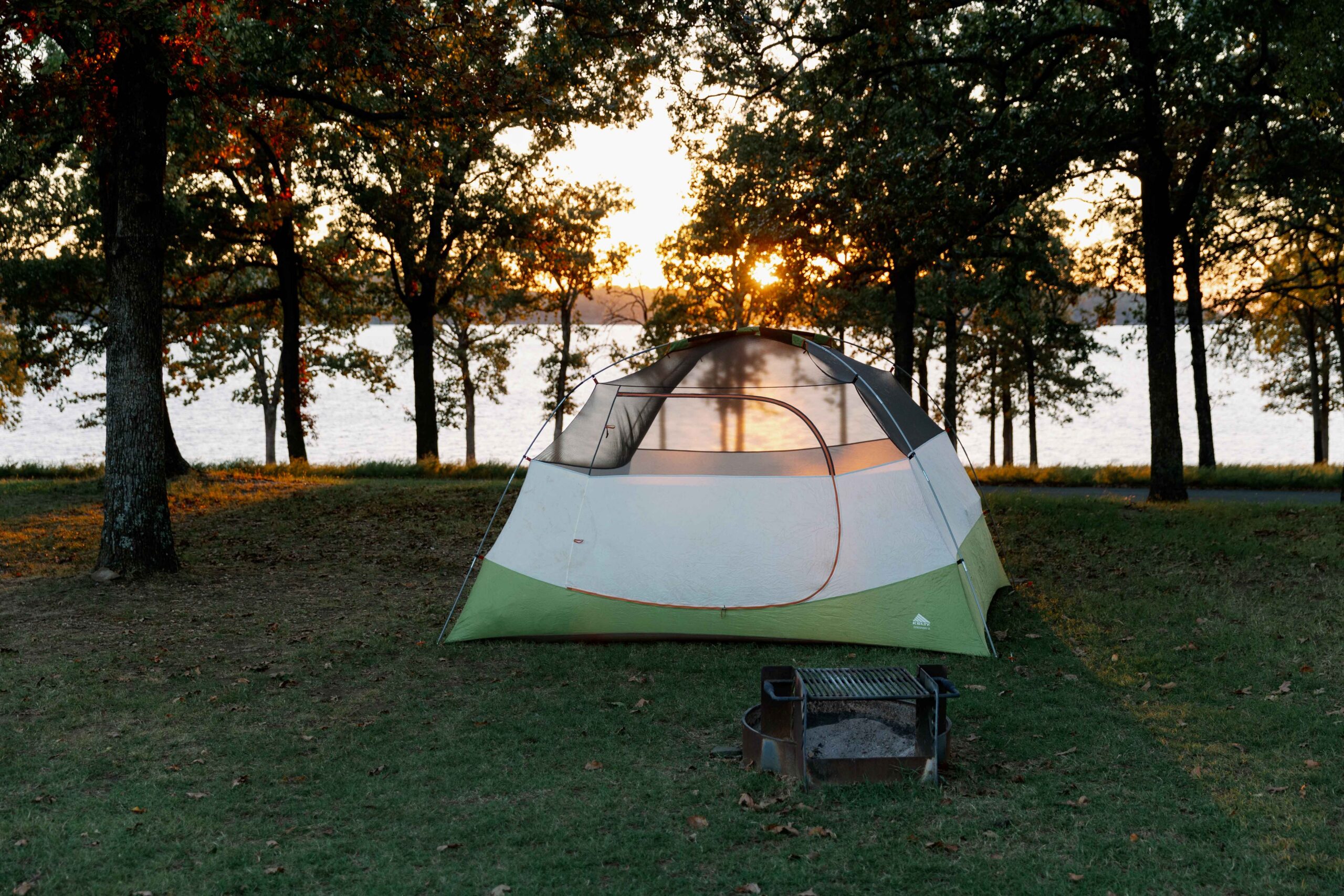 Dome tent pitched under tall pines overlooking the lake at sunset